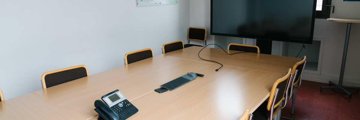 Salle avec table, chaises, écran, téléphone et boitier.