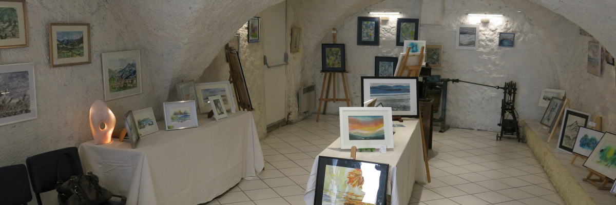 Salle voûtée avec tableaux, chevalets, tables et chaises.