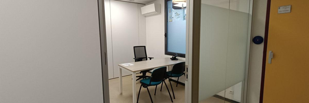 Bureau avec table, chaises, ordinateur, porte vitrée et climatiseur.