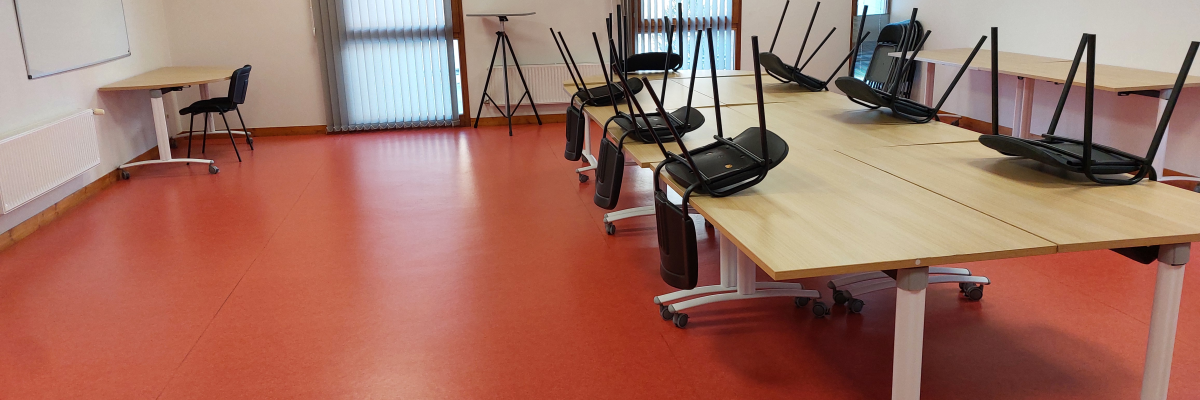 Salle avec table, chaises, tableau blanc, trépied et fenêtres.