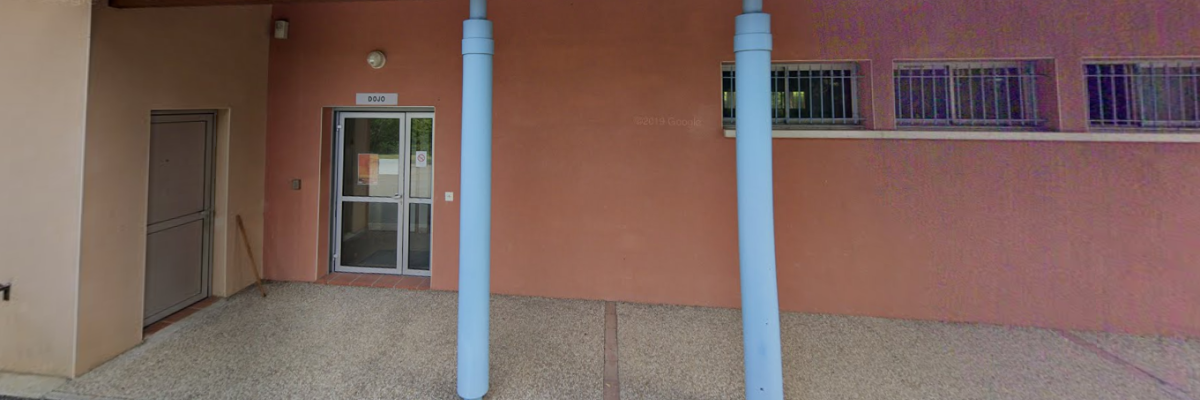 Bâtiment avec porte, fenêtres grillagées, auvent, colonnes bleues.