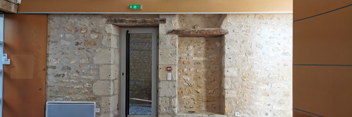 Pièce avec murs en pierre, porte vitrée, radiateur et éclairage au plafond.