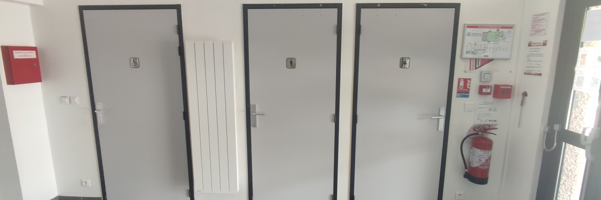 Couloir avec portes, radiateur, extincteur et panneaux d'instructions.