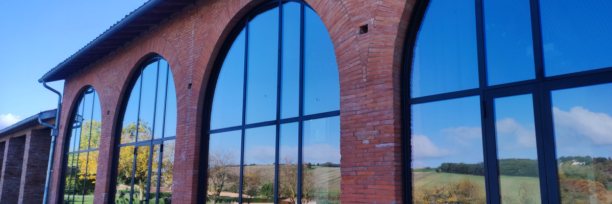 Bâtiment avec grandes fenêtres en arc et briques apparentes, vue sur paysage extérieur.