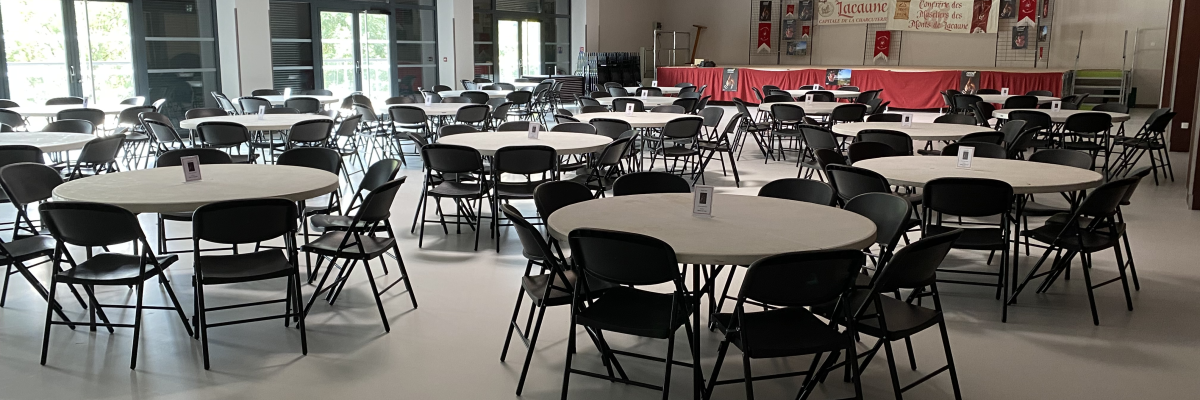 Salle avec tables rondes, chaises, estrade et bannières.
