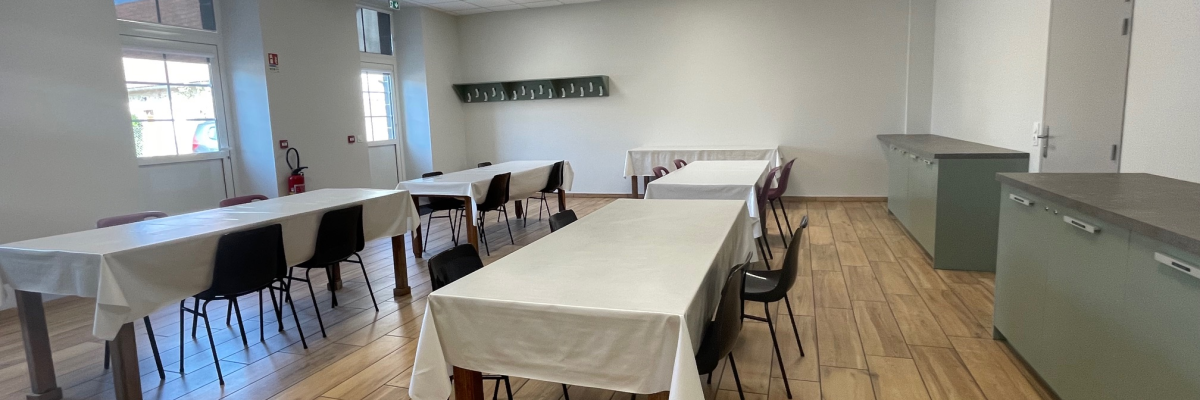 Salle avec tables, chaises, nappes, et meubles de rangement.