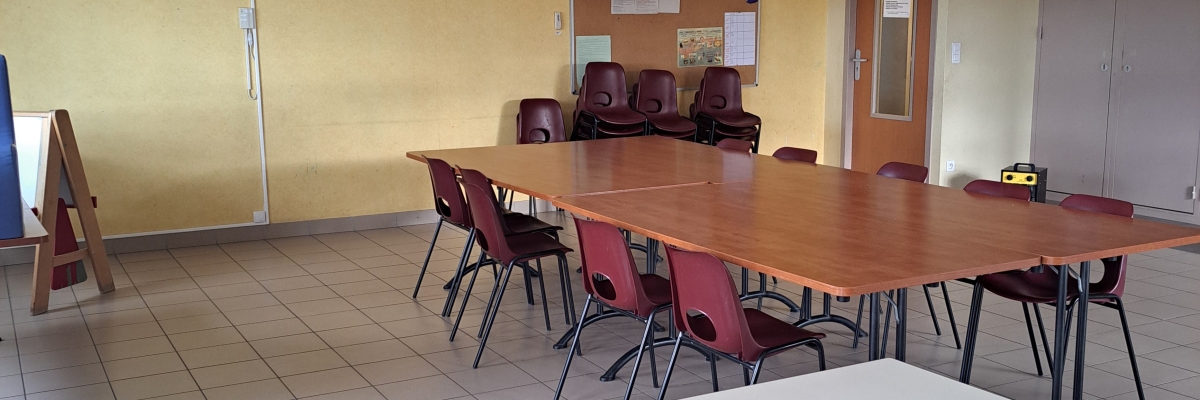 Salle avec tables, chaises, tableau blanc, porte-manteau et lustre.