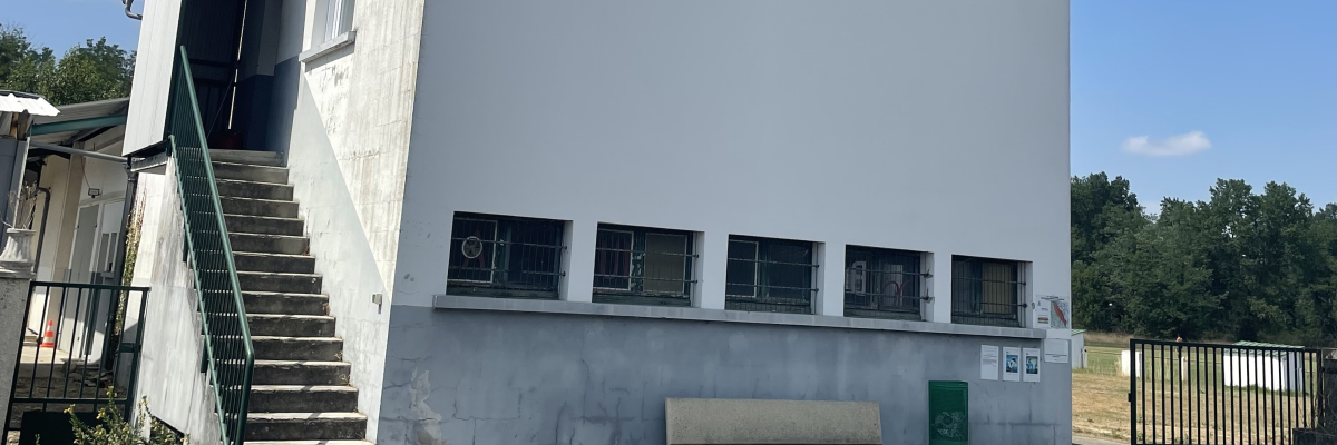 Bâtiment blanc avec escalier extérieur, banc et grillage.