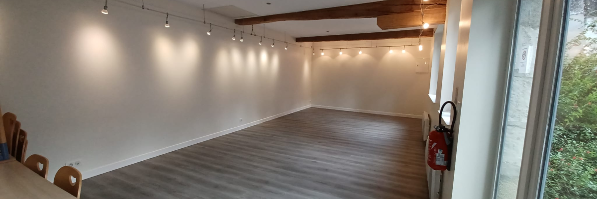 Salle vide avec éclairages, table, chaises enfants et extincteur.