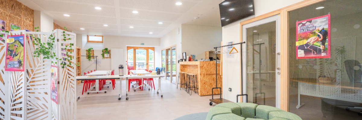 Espace de travail avec tables, chaises, plantes, canapés, écran, porte-manteau et affiches.