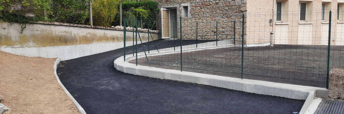 Bâtiment avec revêtement en béton et terrain de sport clôturé.