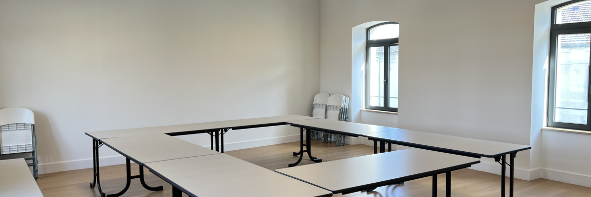 Salle avec tables rectangulaires, chaises, lustres, fenêtres.