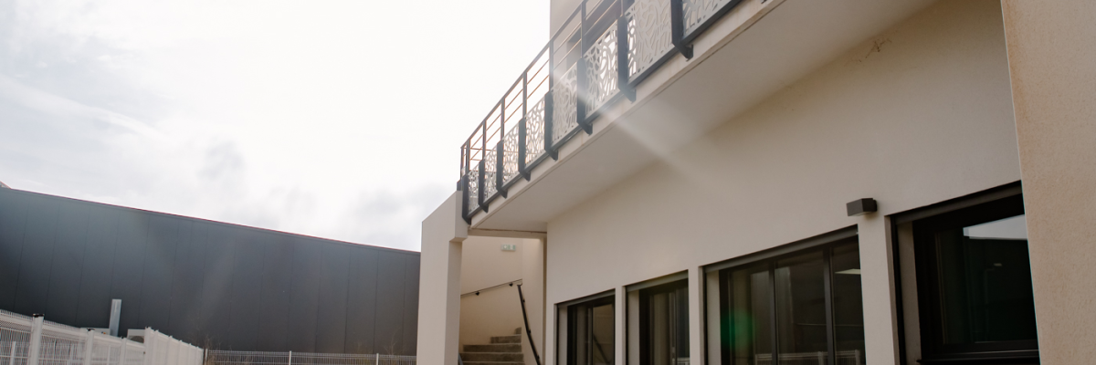 Bâtiment moderne avec terrasses, fenêtres et escalier extérieur. Entrée avec rampes et portails.