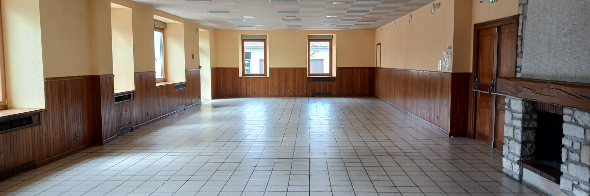 Salle spacieuse avec carrelage, boiseries, fenêtres, plaques chauffantes, cheminée et plafonnier.