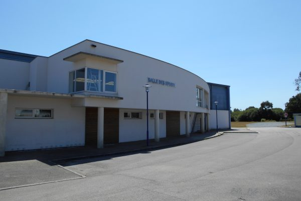 Bâtiment avec enseigne "Salle des Fêtes", parking vide, ciel dégagé.
