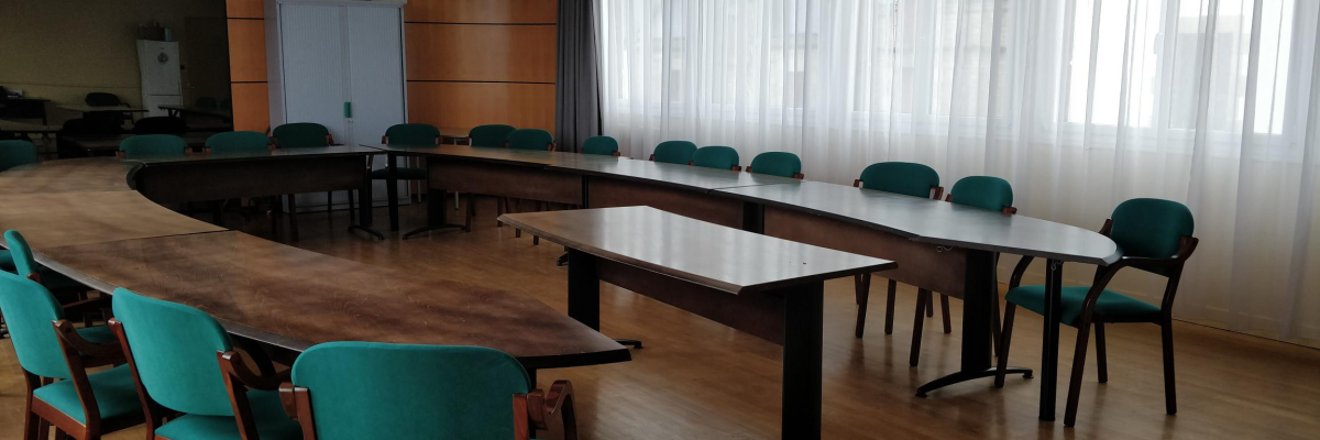 Salle de réunion avec tables, chaises, armoire et climatiseur.