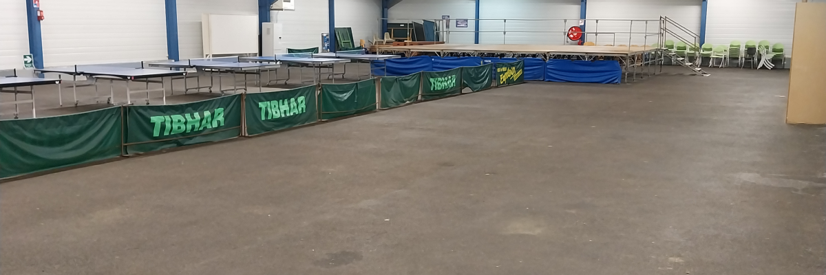 Salle spacieuse avec trampolines, sol en béton, murs blancs et plafond haut éclairé.