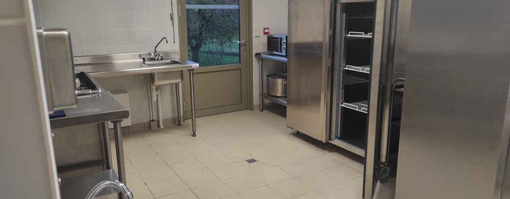 Cuisine équipée : évier, plan de travail, frigo, porte ouverte, fenêtre.