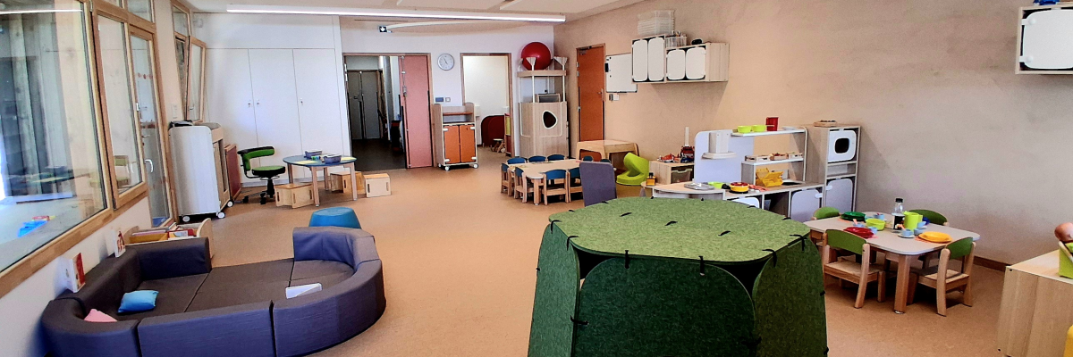 Salle avec canapés, tables, chaises, tentes et jouets.