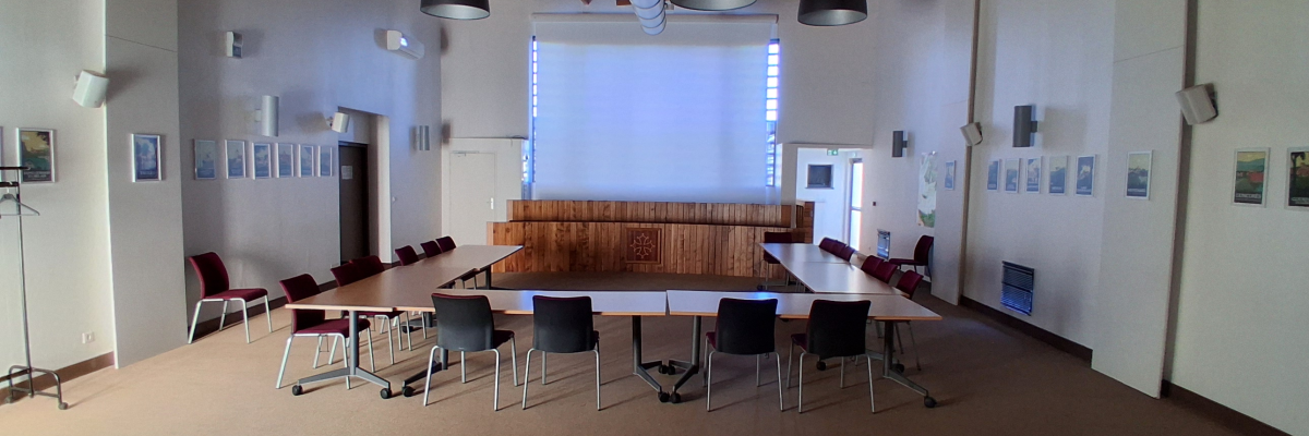 Salle avec tables, chaises, écran, suspensions lumineuses et tableau d'affichage.