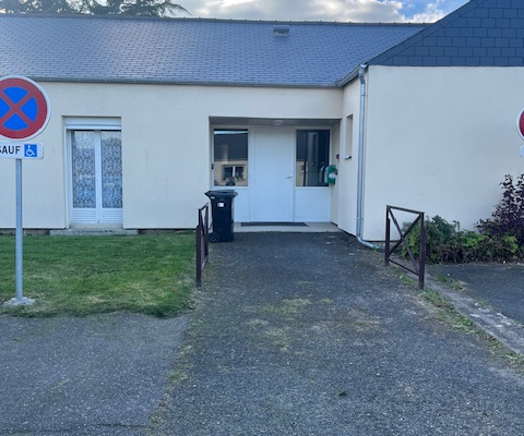 Bâtiment avec entrée, poubelles, panneaux de signalisation, pelouse et allée en asphalt.