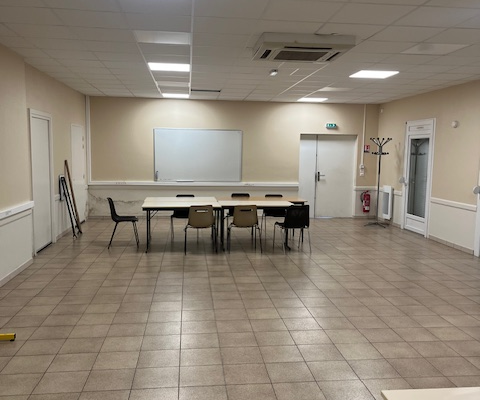 Salle vide avec table, chaises, tableau blanc, climatiseur, porte et étagères.