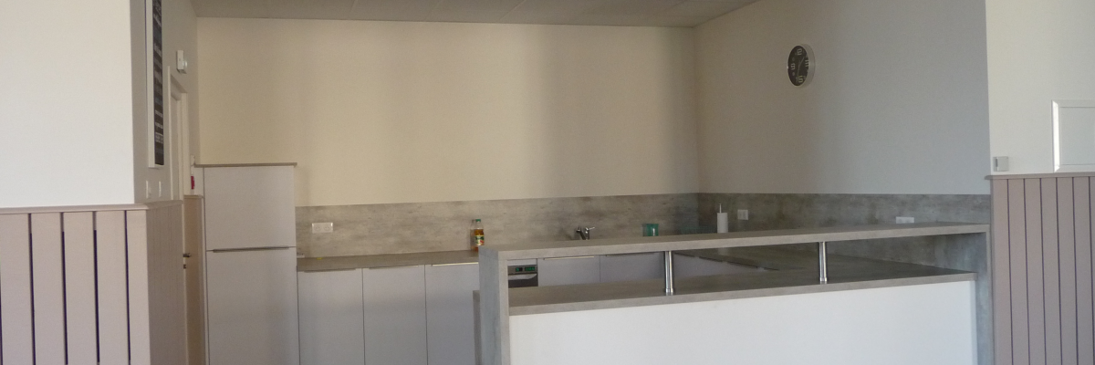 Cuisine avec plan de travail, éviers, réfrigérateur et horloge.