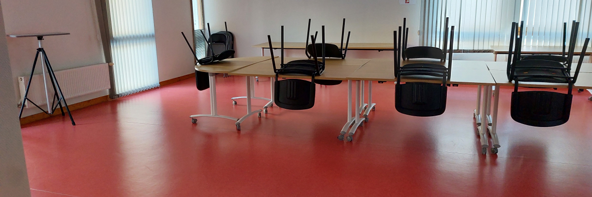 Salle avec tables, chaises, projecteur sur trépied et fenêtres.