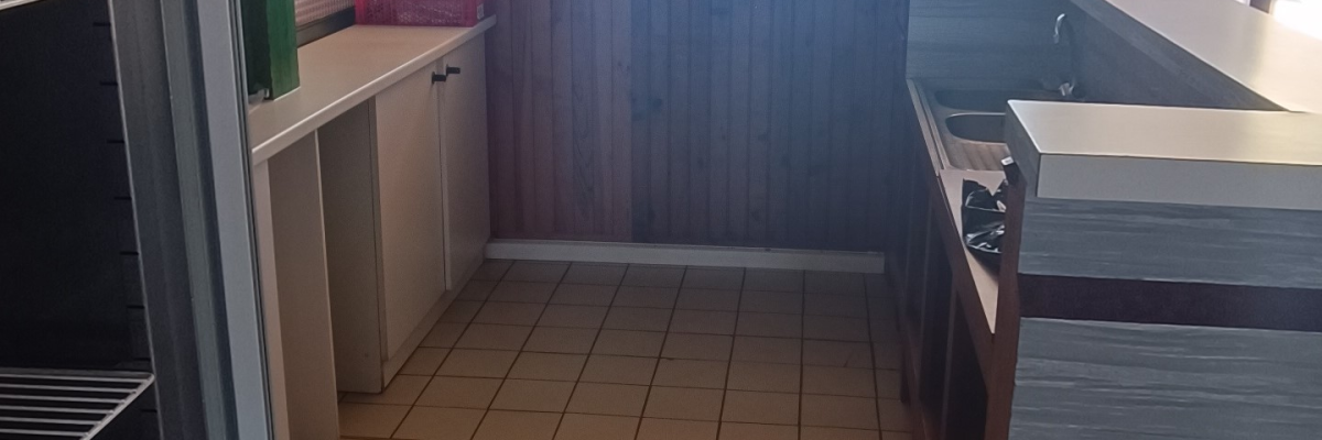 Cuisine avec plans de travail, meubles bas, sol carrelé et étagères.