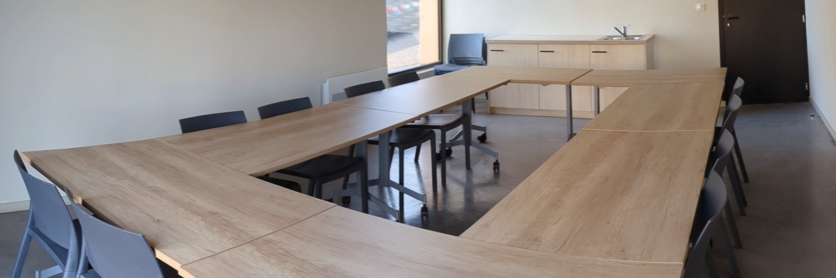 Salle avec table rectangulaire, chaises bleues, porte et fenêtre.