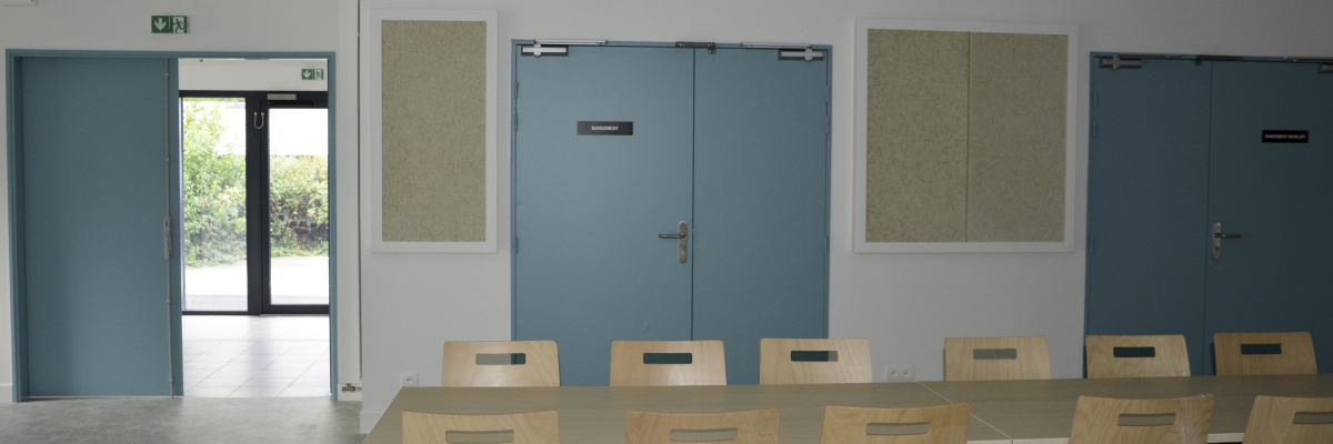Salle avec table, chaises, portes et sortie de secours.