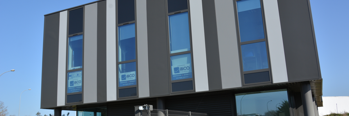 Bâtiment avec façade en bandes verticales grises et blanches, fenêtres, enseignes, entrée vitrée, barrière, panneau d'interdiction de stationner et voiture stationnée.