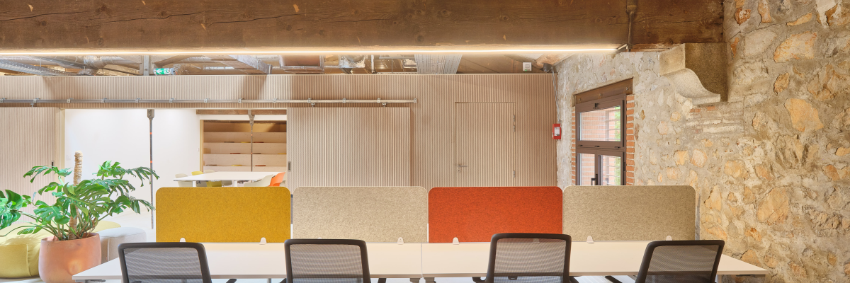 Salle de réunion avec table, chaises, murs en brique, ventilation apparente et plantes.