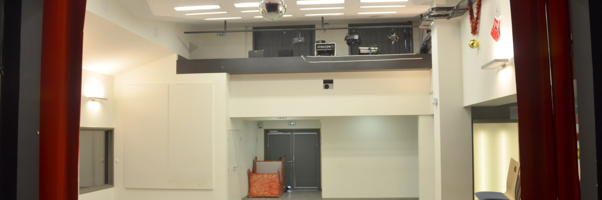 Salle vide avec projecteur, écrans, et haut-parleurs suspendus.