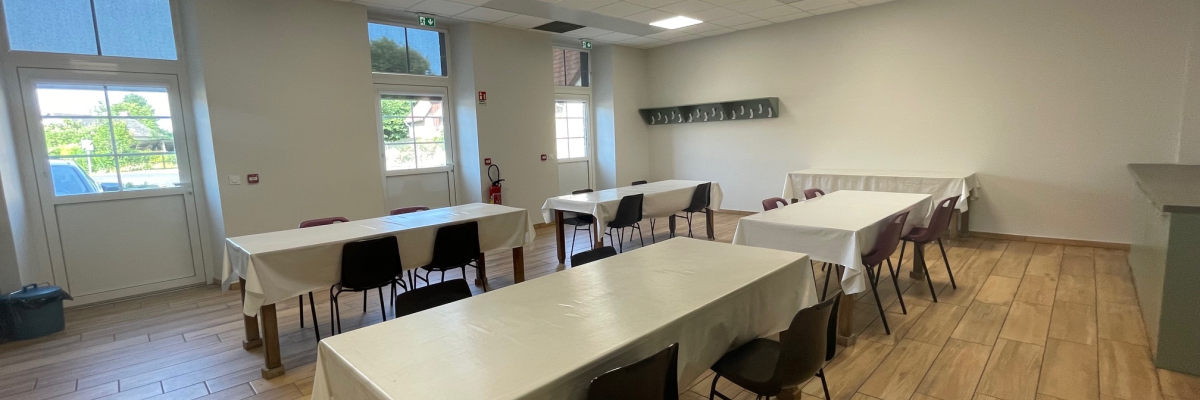 Salle avec tables, chaises, nappes blanches et lumière naturelle.