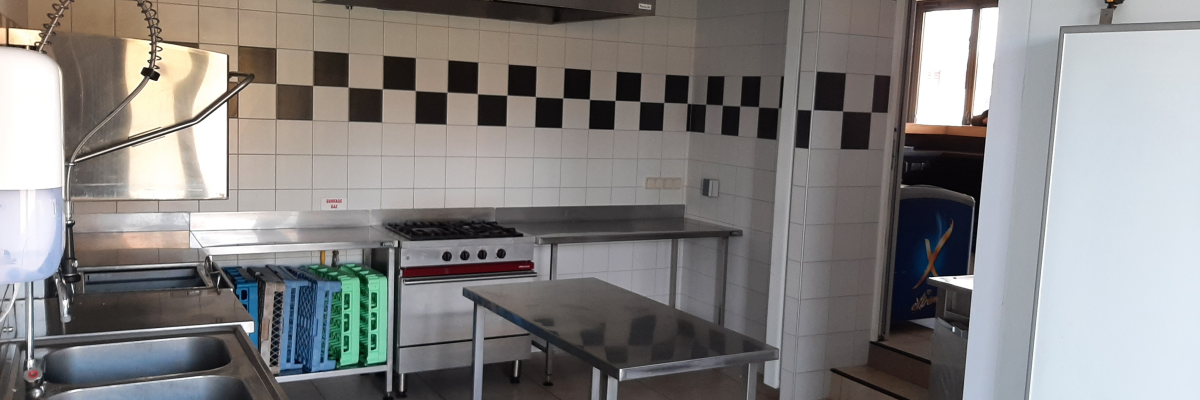 Cuisine avec plans de travail, éviers, plaques de cuisson, étagères à plateau et hottes.