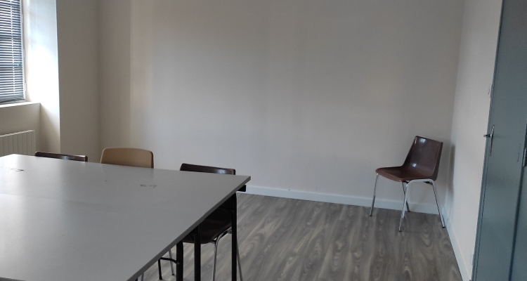 Pièce avec table, chaises, sol en bois, porte verte et fenêtre.