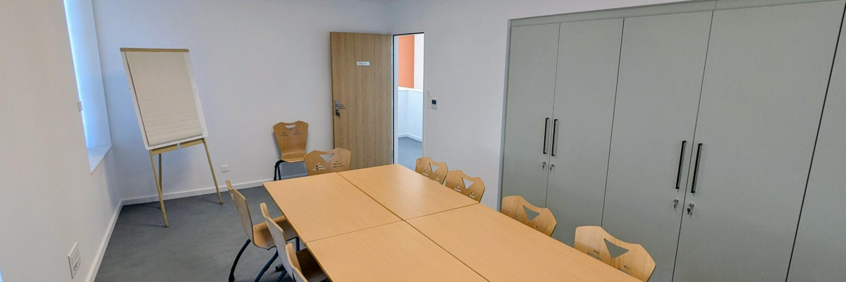 Salle de réunion avec table, chaises, tableau blanc, armoire et porte.