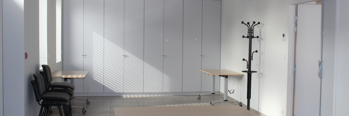 Salle vide avec tables, chaises, porte-manteau et armoires.