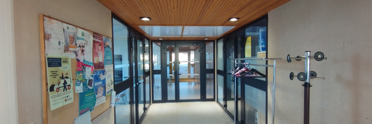 Couloir avec plafond en bois, tableau d'affichage, porte-manteau et porte vitrée.