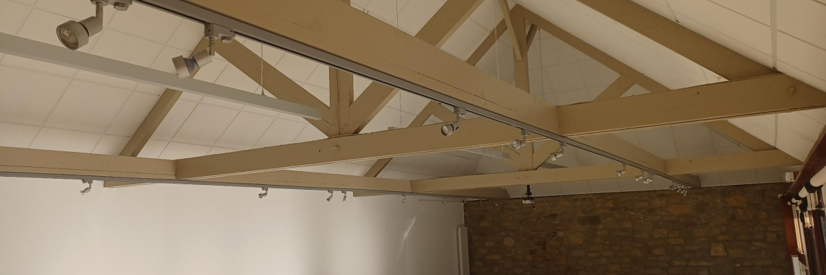 Salle avec poutres apparentes, chaises empilées, table, et mur de briques.