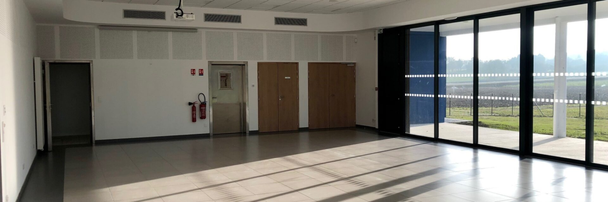 "Grande salle vide avec portes, fenêtres, extincteur, et plafond suspendu."