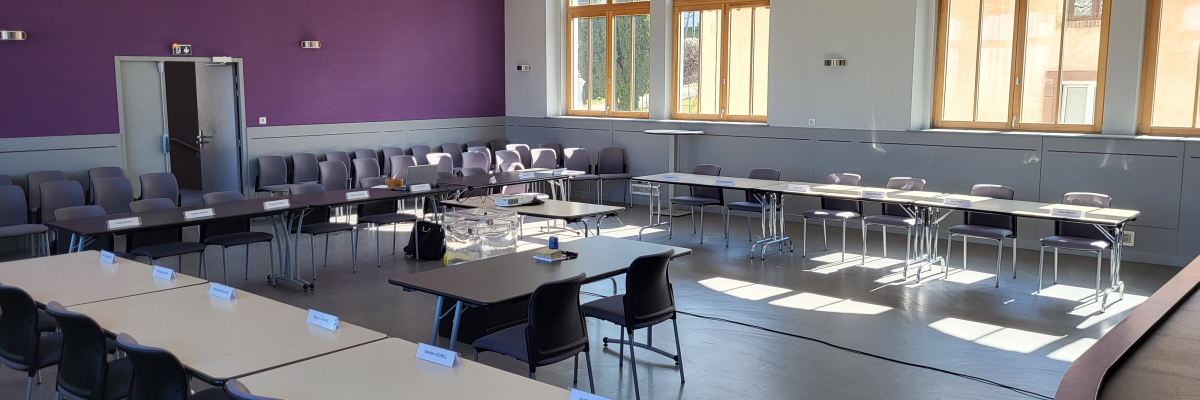 Salle de classe avec tables, chaises, télévision et fenêtres.