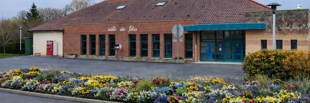 Bâtiment avec toiture en tuiles, murs en brique, grandes fenêtres, entrée avec auvent bleu, panneau de signalisation, parterre de fleurs.