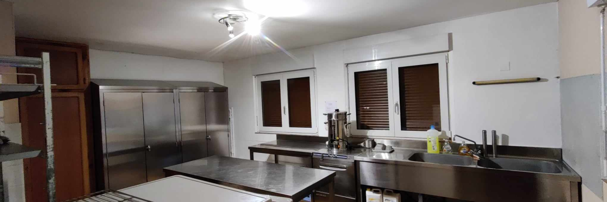 Cuisine avec plans de travail, évier, réfrigérateur, fours, étagères et fenêtres.