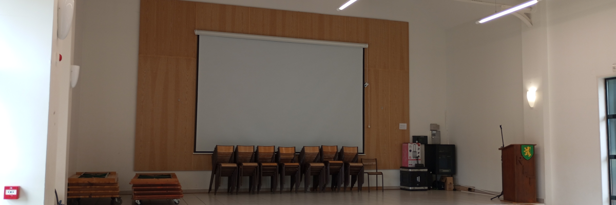 Salle avec écran, chaises, pupitre, projecteur et matériel audio.