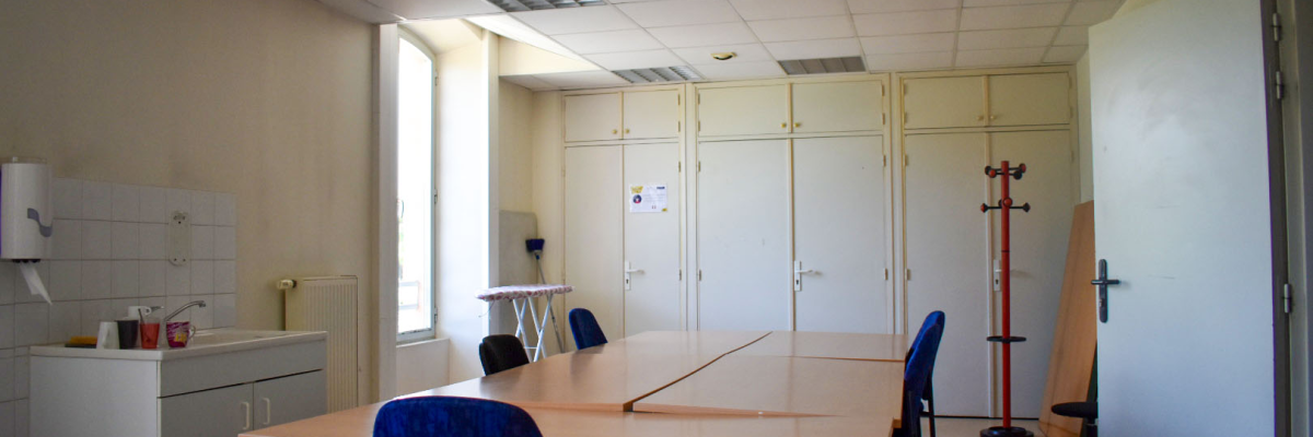 Salle de réunion avec table, chaises, armoires, porte-manteaux, évier, table de préparation.