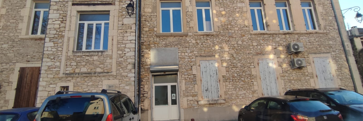 Batiment en pierre avec entrée, trois voitures et lampadaire.