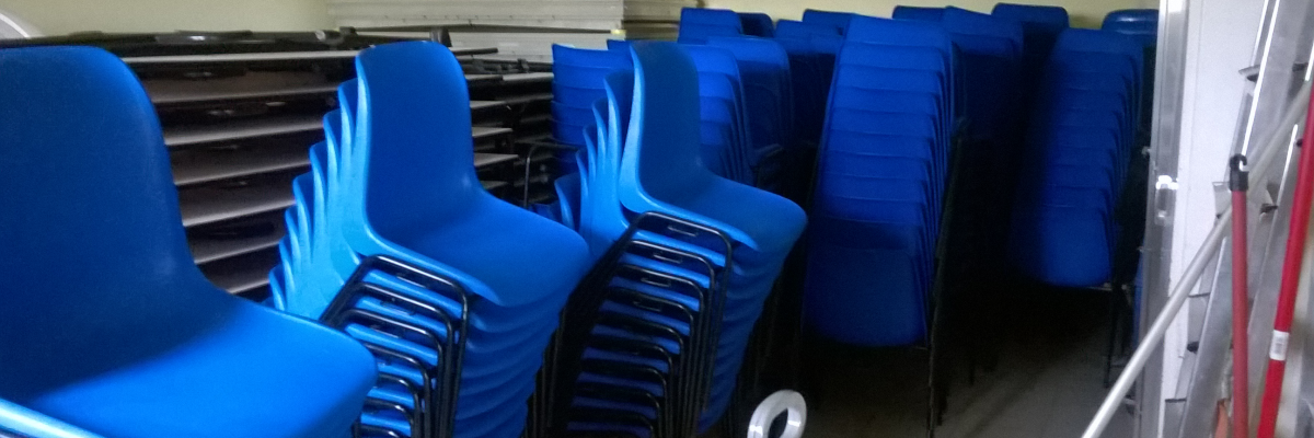 Pièces empilées, chaises bleues, tablettes, balai.