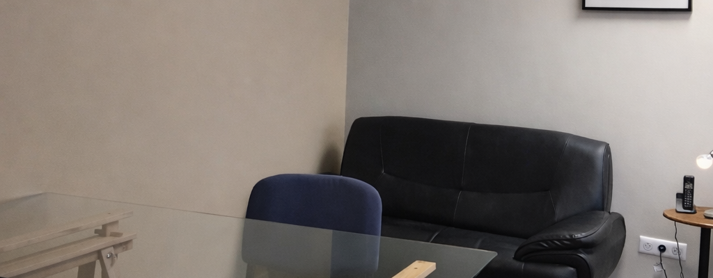 Salle avec canapé, table en verre, chaises pliantes et table de travail.